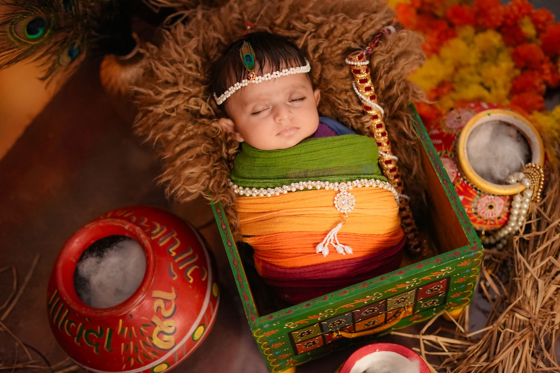 A sleeping baby wrapped in multicolored fabric, adorned with traditional jewelry, surrounded by festive Indian elements.