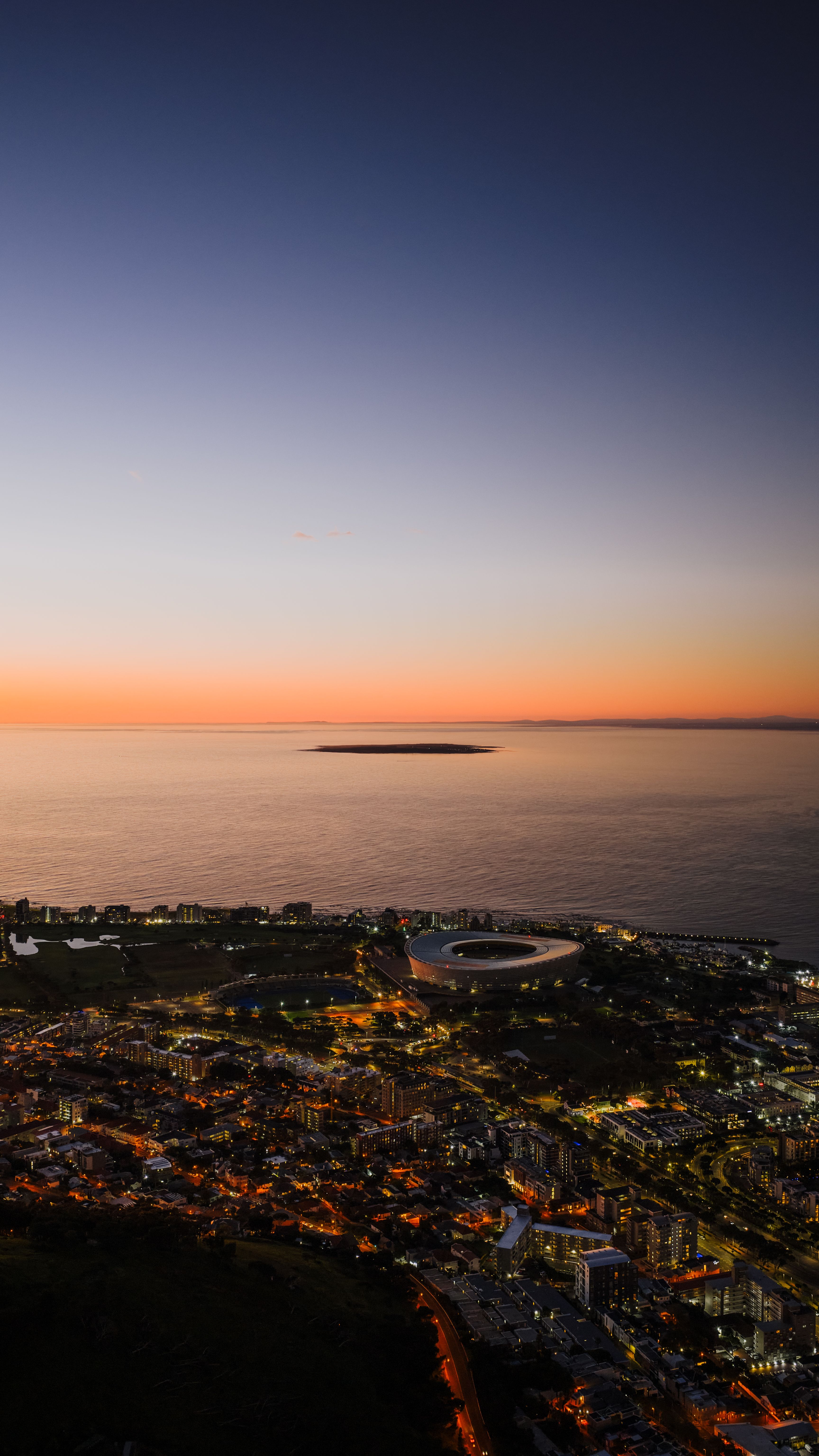 Stunning aerial twilight view of Cape Town, featuring the vibrant city lights against the calm ocean.