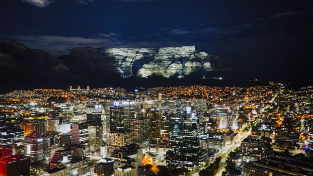 Stunning aerial view of Cape Town's illuminated cityscape with Table Mountain in the background at night.