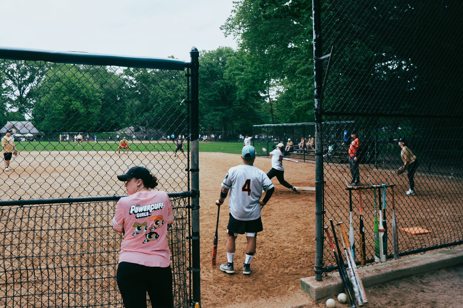 A casual baseball game in a New York City park with players and spectators on a sunny day.