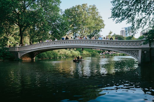 A picturesque scene of Bow Bridge with people and a boat in Central Park, New York City.
