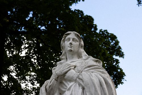 Free A tranquil marble statue captured outdoors with a backdrop of lush trees and clear skies. Stock Photo