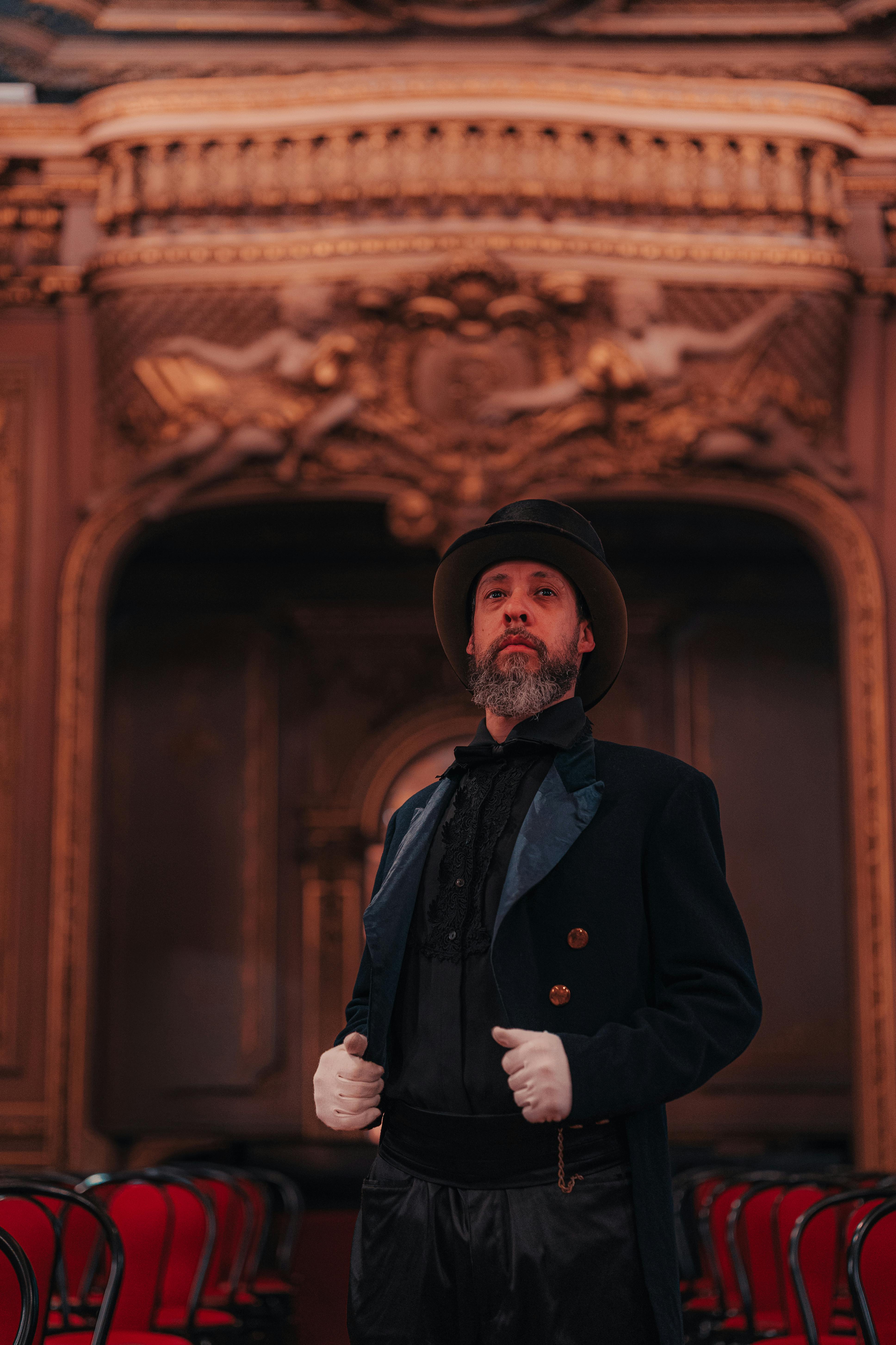 Free A distinguished man in vintage attire poses inside an ornate theater, exuding elegance and sophistication. Stock Photo
