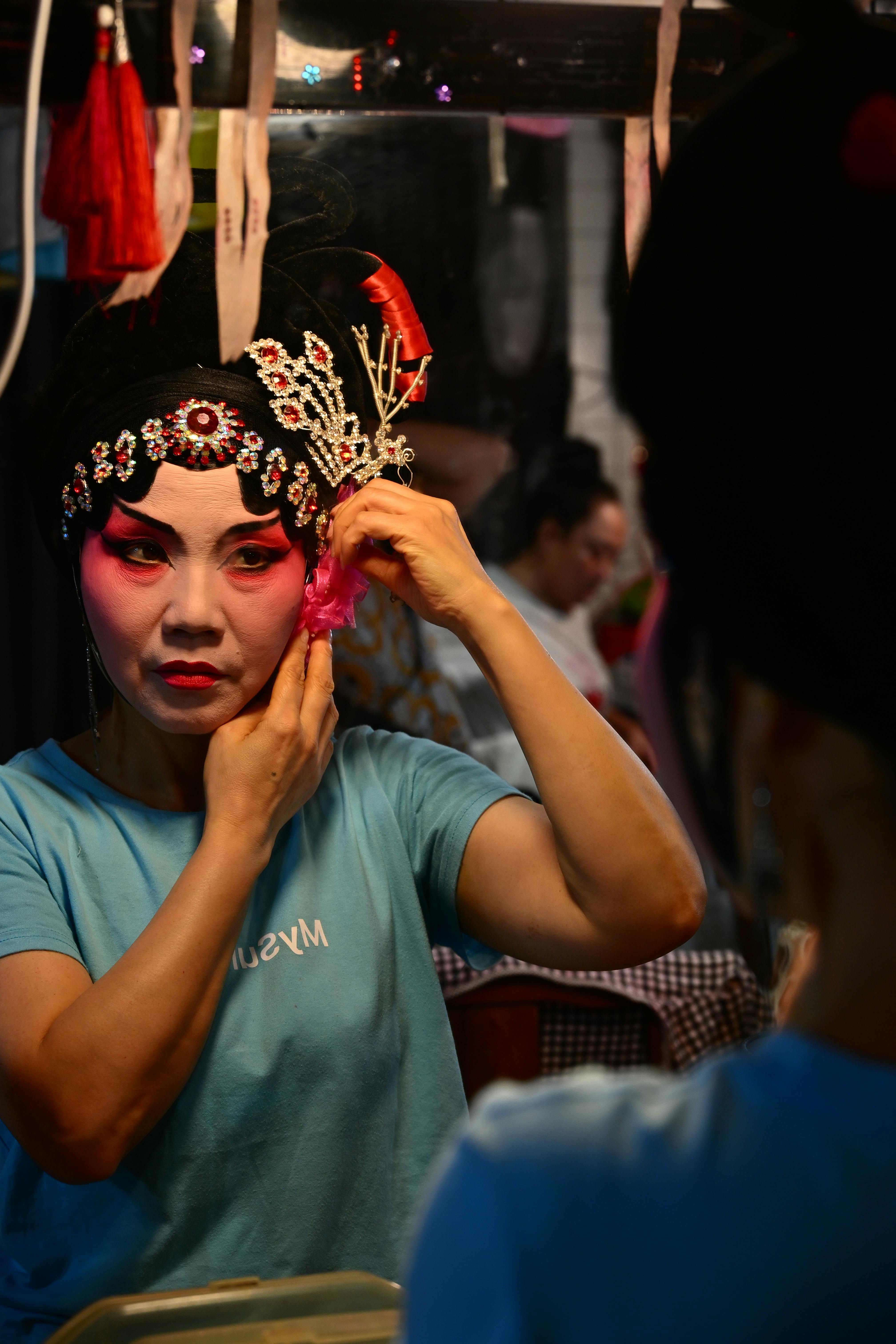 Gratis En skuespillerinde i traditionel kinesisk operamakeup justerer sit hovedbeklædning bag scenen og indfanger et øjeblik med kulturel kunstnerisk dygtighed. Lagerfoto