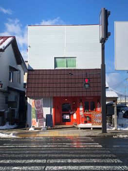 Vibrant red building on a snowy city street in Japan, under a clear blue sky.