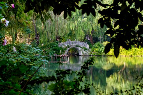 Free A serene landscape featuring a traditional stone bridge over a reflective lake surrounded by lush greenery. Stock Photo