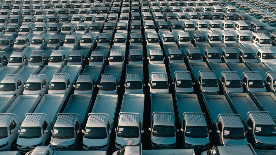 Overhead shot of a large collection of white pickup trucks parked in neat rows, emphasizing industrial scale.