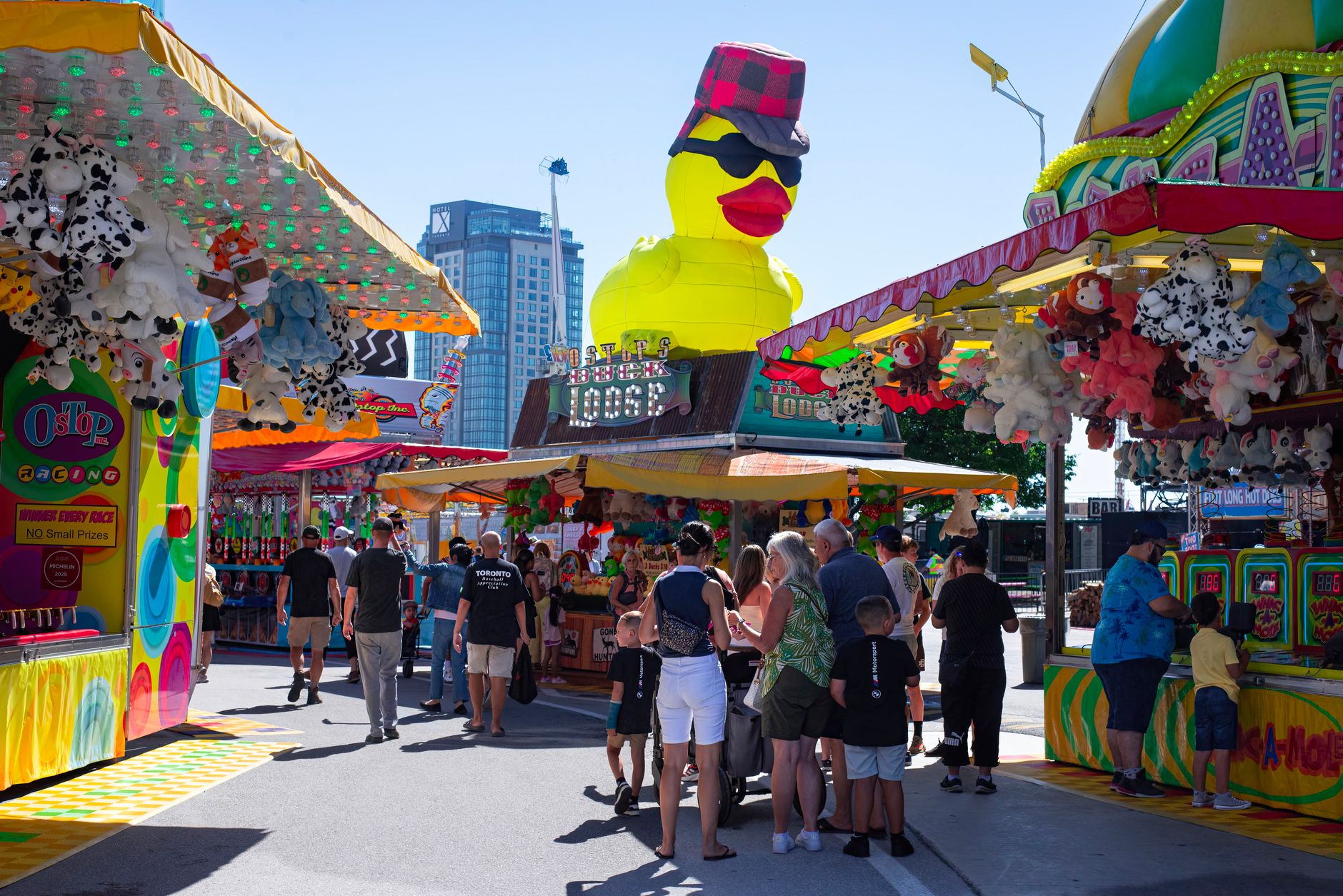 carnival games rental cairo — Colorful summer carnival scene with a giant rubber duck and game stalls under clear blue sky.