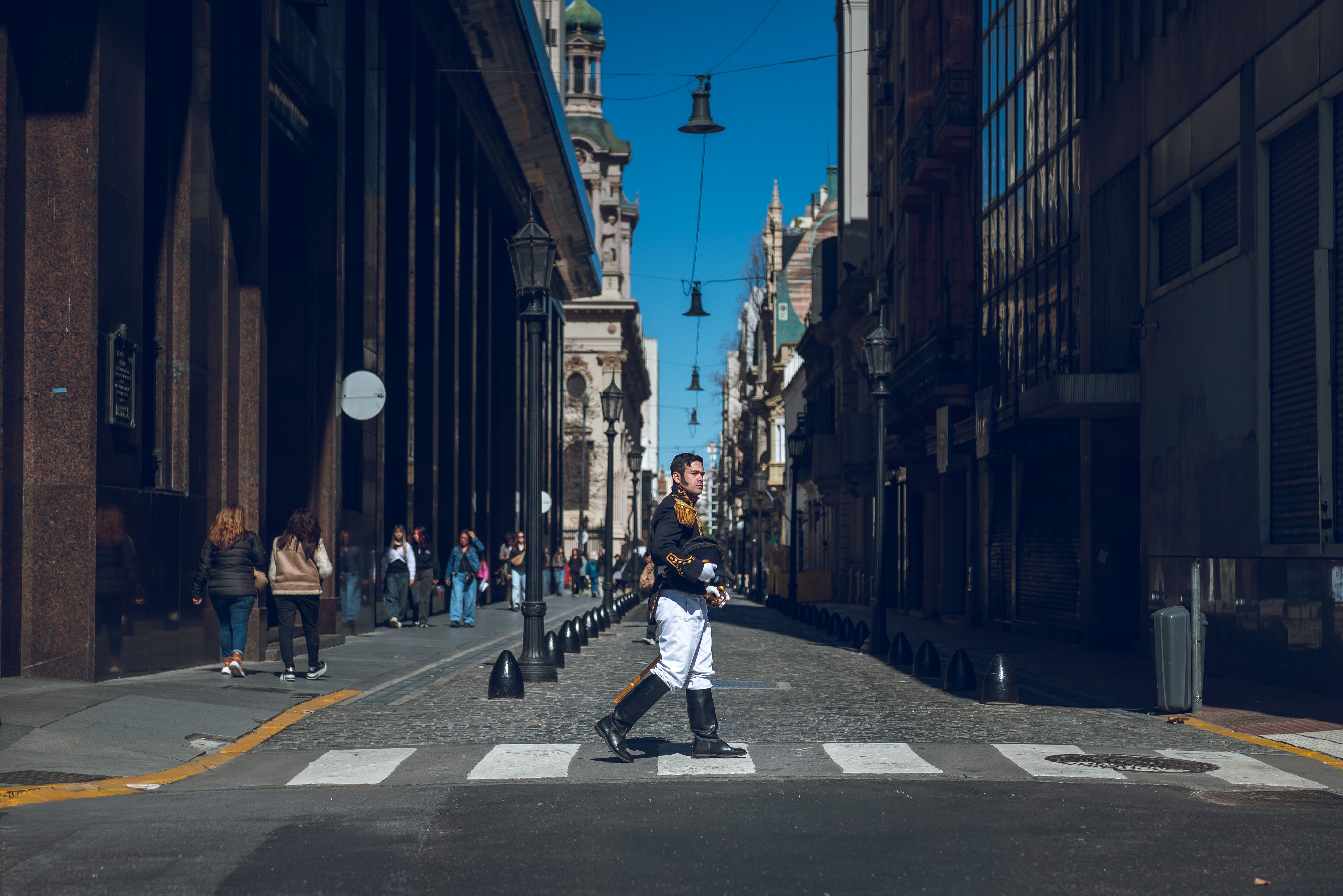 A guard in ceremonial uniform crossing a city street in Buenos Aires on a sunny day.