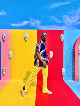 Stylish individual posing against a vivid, colorful background with vibrant wall masks.