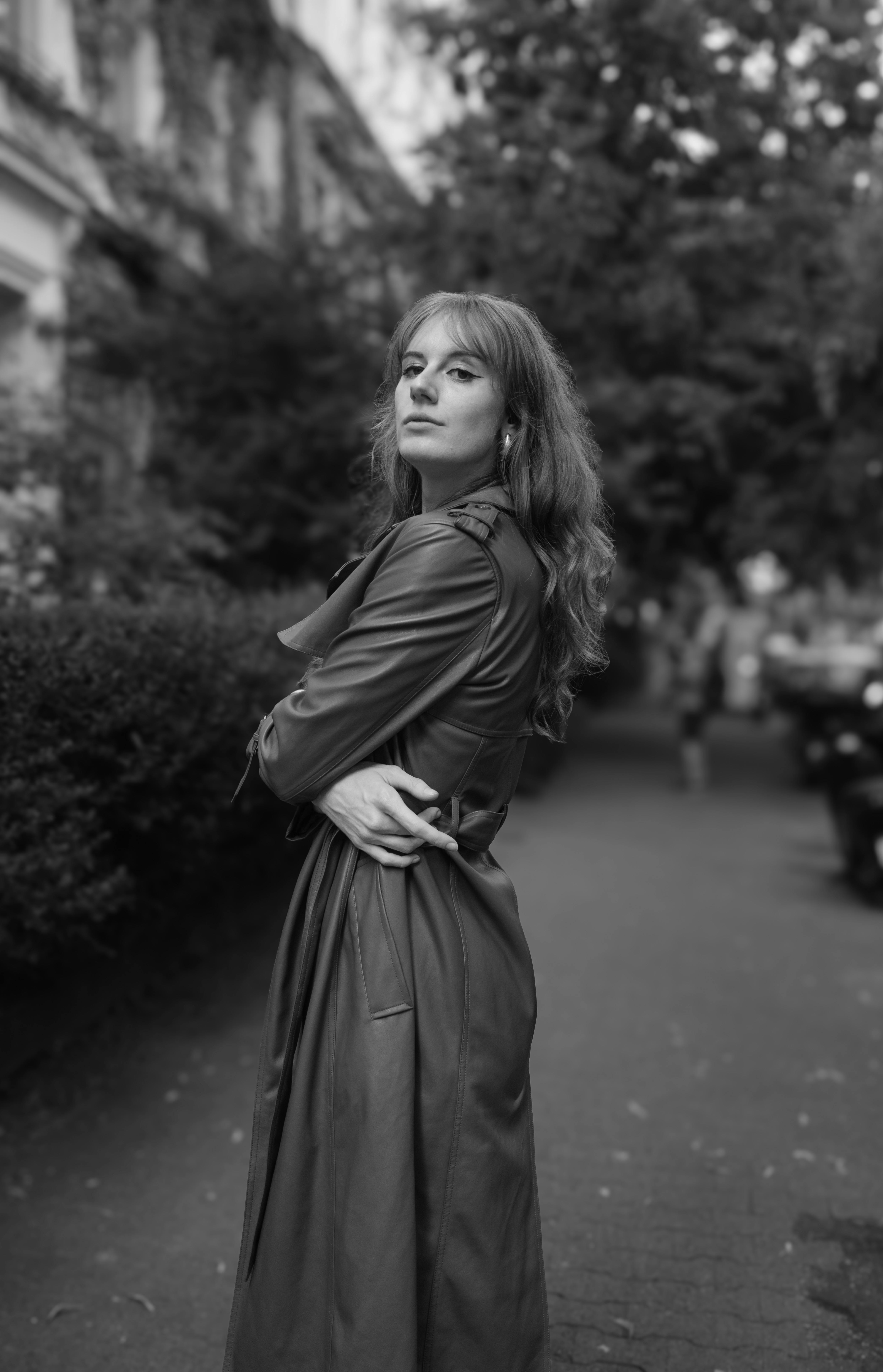 Elegant woman posing in a long coat on a city sidewalk in monochrome.
