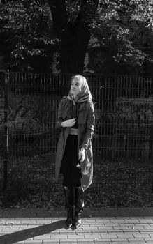 A thoughtful black and white portrait of a woman standing on a sidewalk.