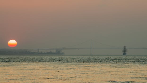 A serene sunrise view over Lisbon's iconic 25 de Abril Bridge and calm sea.