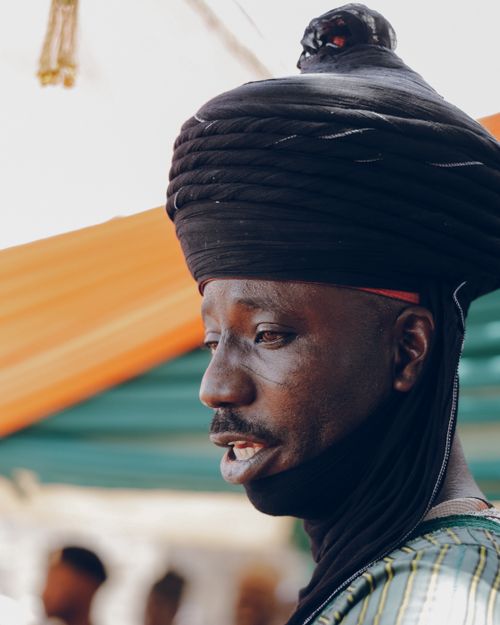 Free Close-up portrait of a man wearing traditional African headwear under a colorful canopy at an outdoor event. Stock Photo