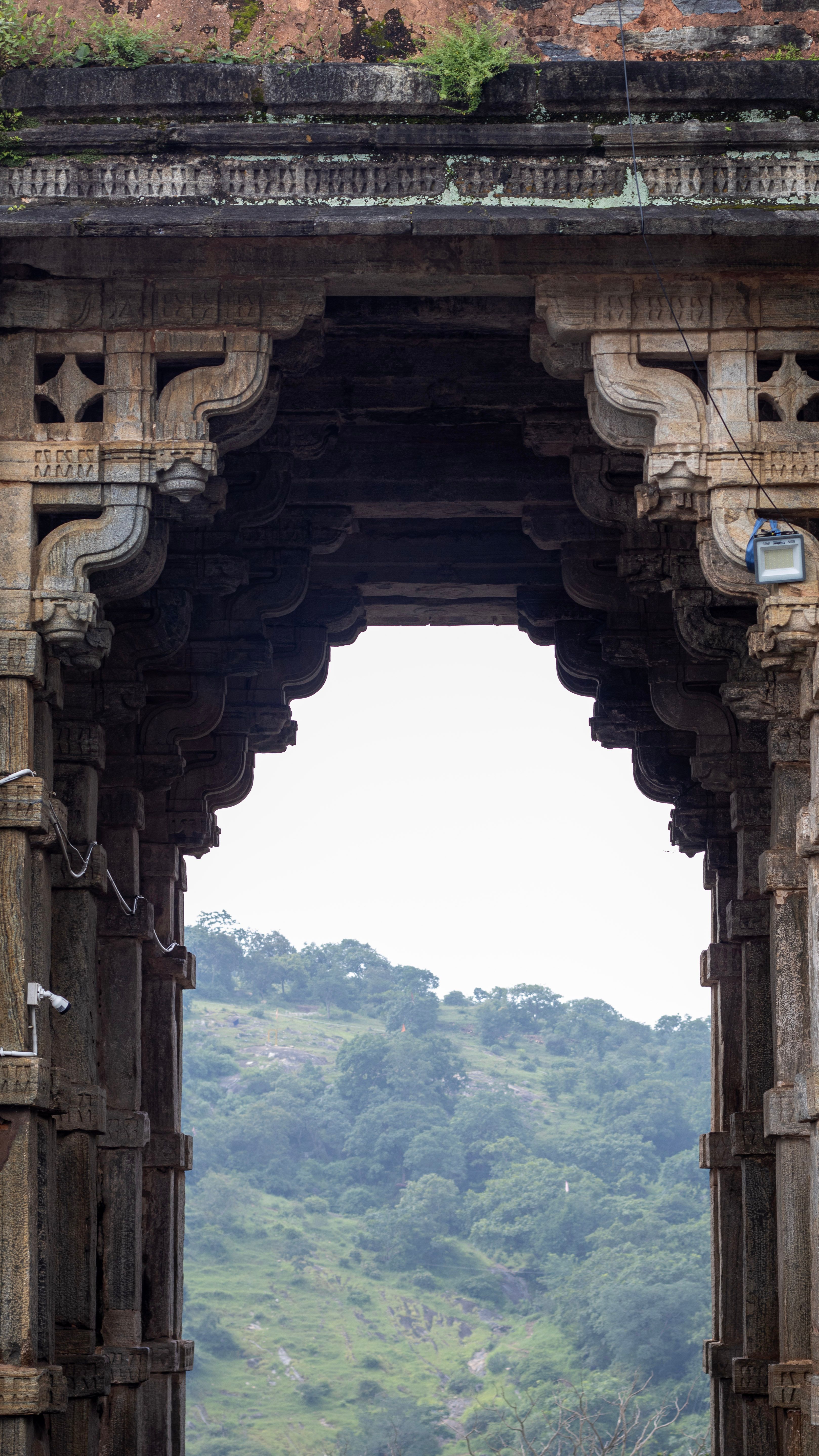 Historic stone archway in Udaipur, Rajasthan offering a scenic view of lush hills.