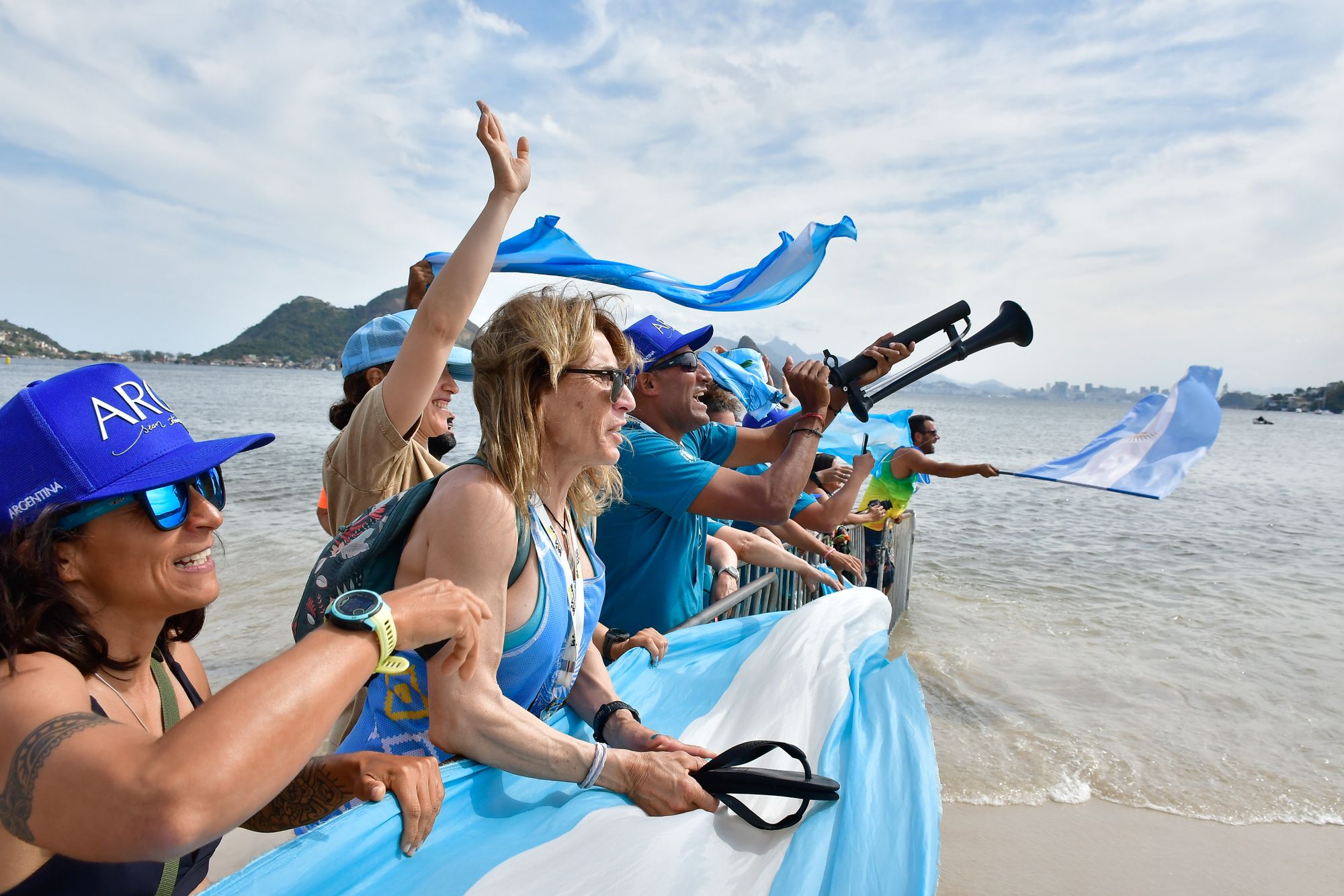 Excited crowd waving flags and cheering by the beach in Niterói, Brazil.