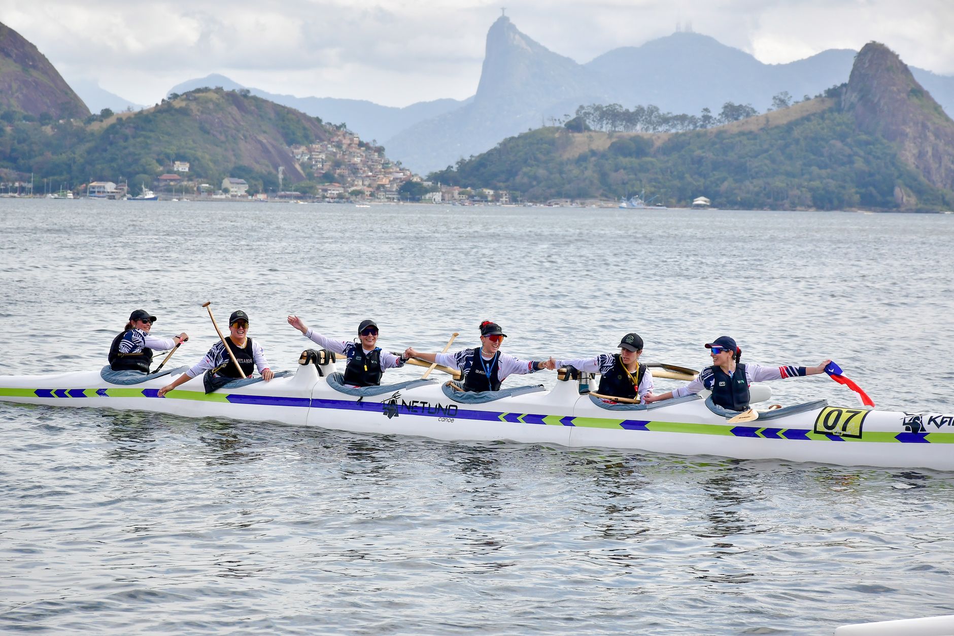 A group of young adults canoeing in Rio de Janeiro, Brazil with scenic mountain views.