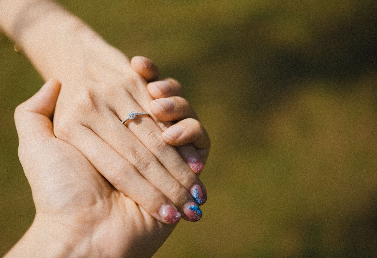 a close up image of a hand wearing an engagement ring with colorful na