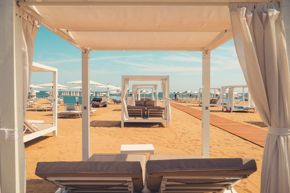 White beach cabanas with tied-back curtains and paired loungers along a boardwalk