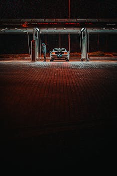 晚上，一名男子站在加油站的一辆汽车旁，被人造灯光照亮