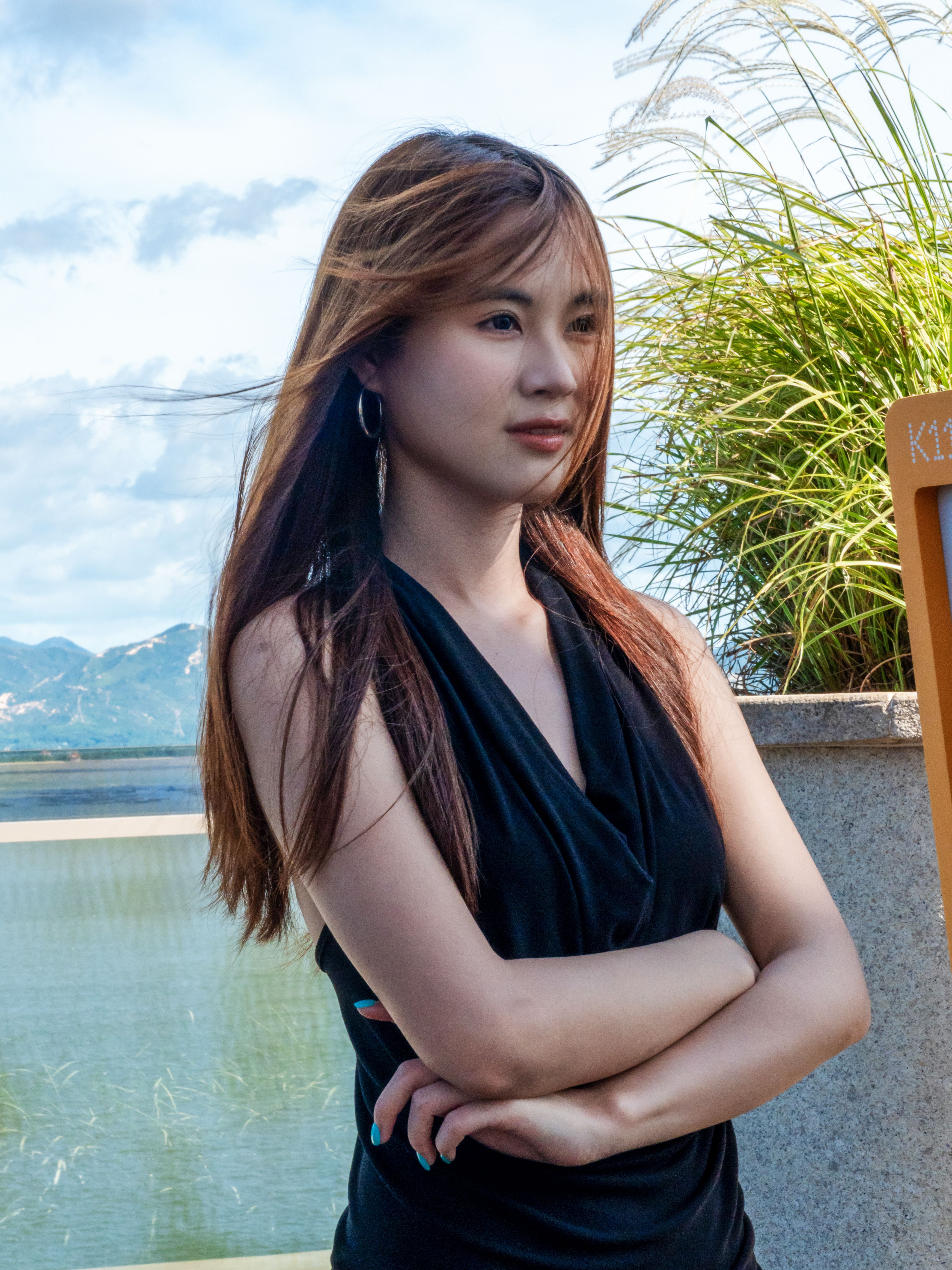A young woman stands gracefully by the water, scenic mountains in Shenzhen.