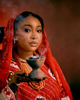Portrait of a woman in vibrant African attire holding burning incense, showcasing cultural heritage.