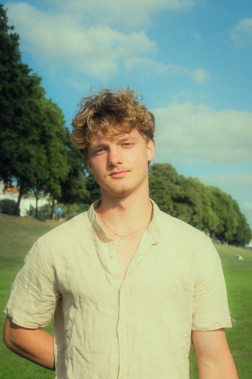 Free A young male model poses outdoors in a sunny park, exuding a relaxed, dreamy vibe. Stock Photo