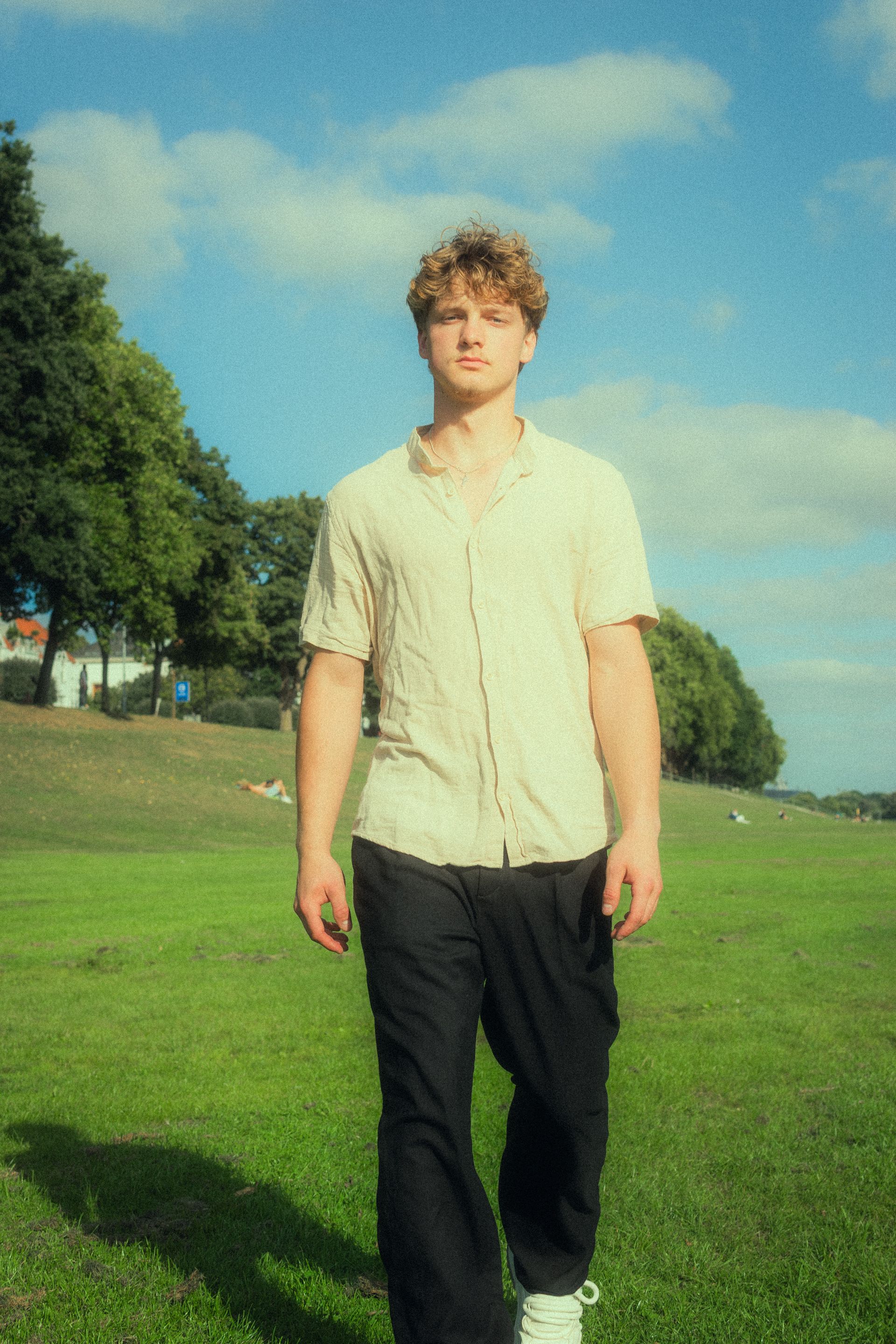 Young man in casual dress walking in a sunny park setting, summer vibes.