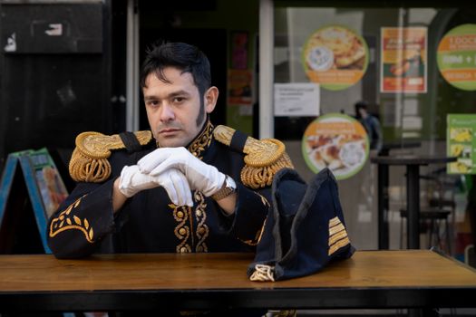 Man dressed in ornate historical uniform sits at an outdoor cafe table in Buenos Aires.