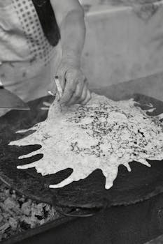 Monochrome image of cooking flatbread on an outdoor griddle, showcasing texture and detail.