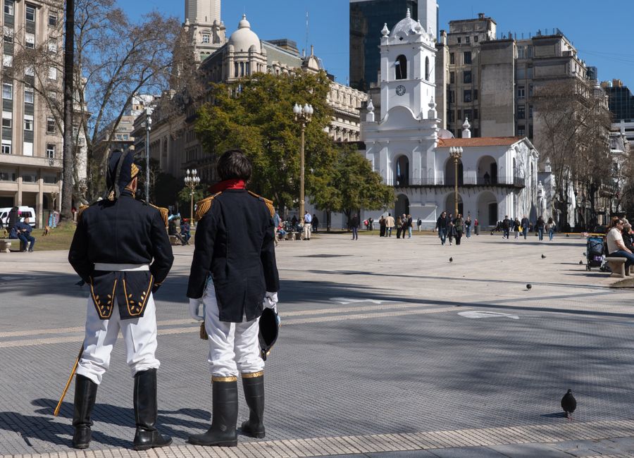 Two reenactors in historical military uniforms at iconic Buenos Aires plaza with Cabildo.