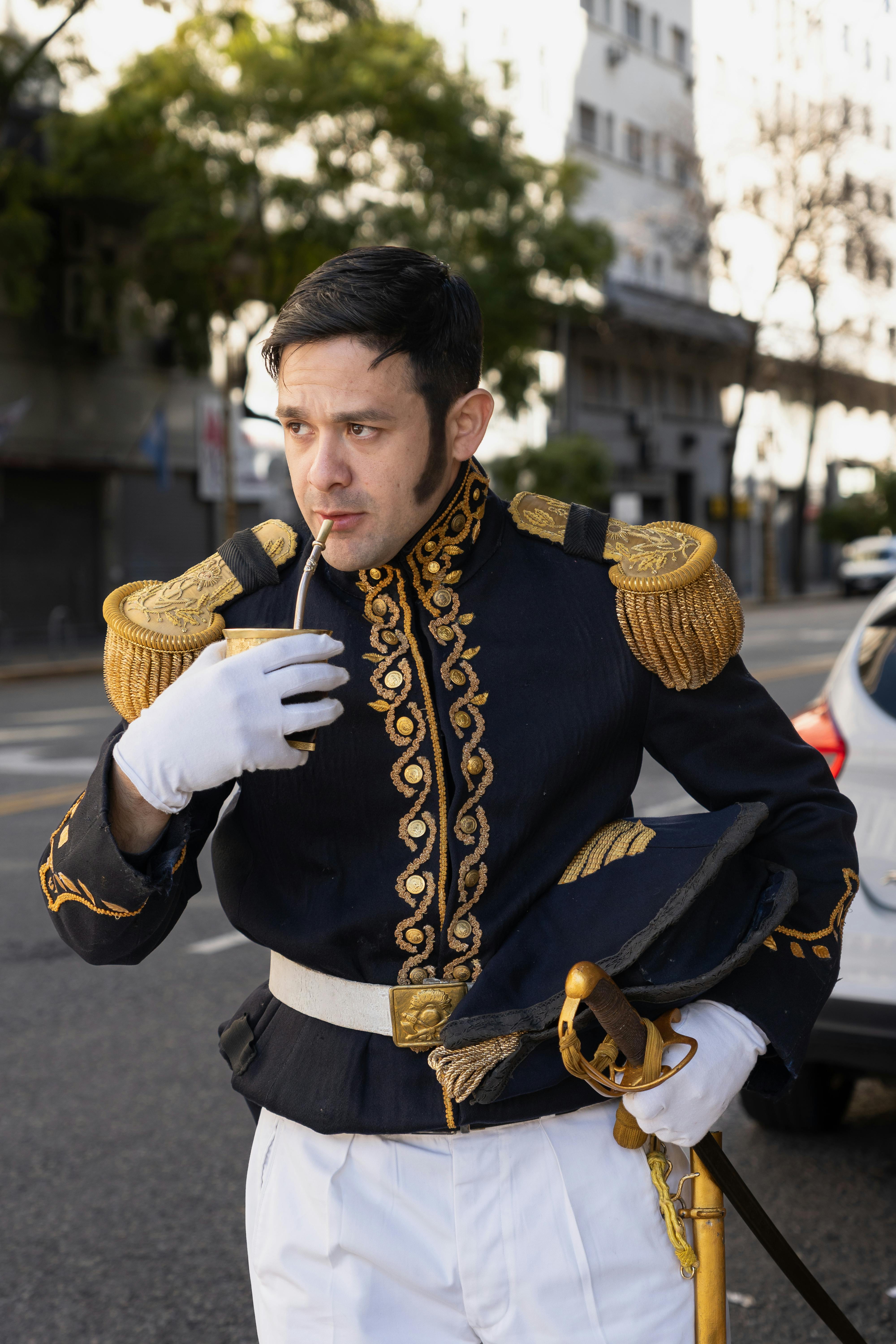 Man in ornate historical uniform drinks mate on Buenos Aires street.