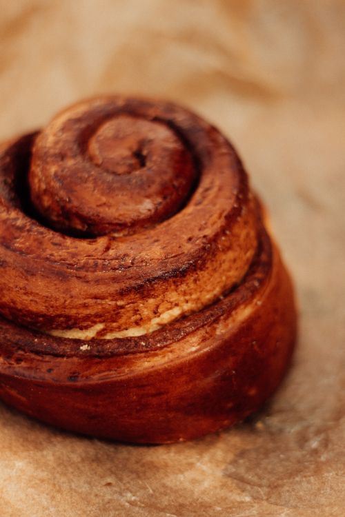 Free Warm, fresh cinnamon roll captured in detail on parchment paper, perfect for food lovers. Stock Photo