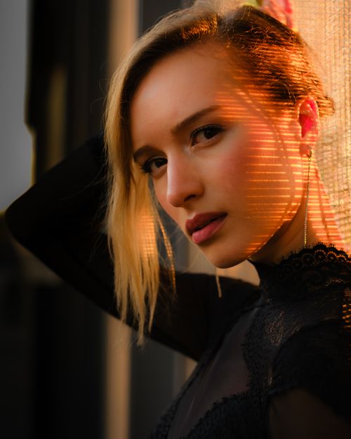 Free Stylish portrait of a young woman illuminated by warm sunset light through blinds. Stock Photo