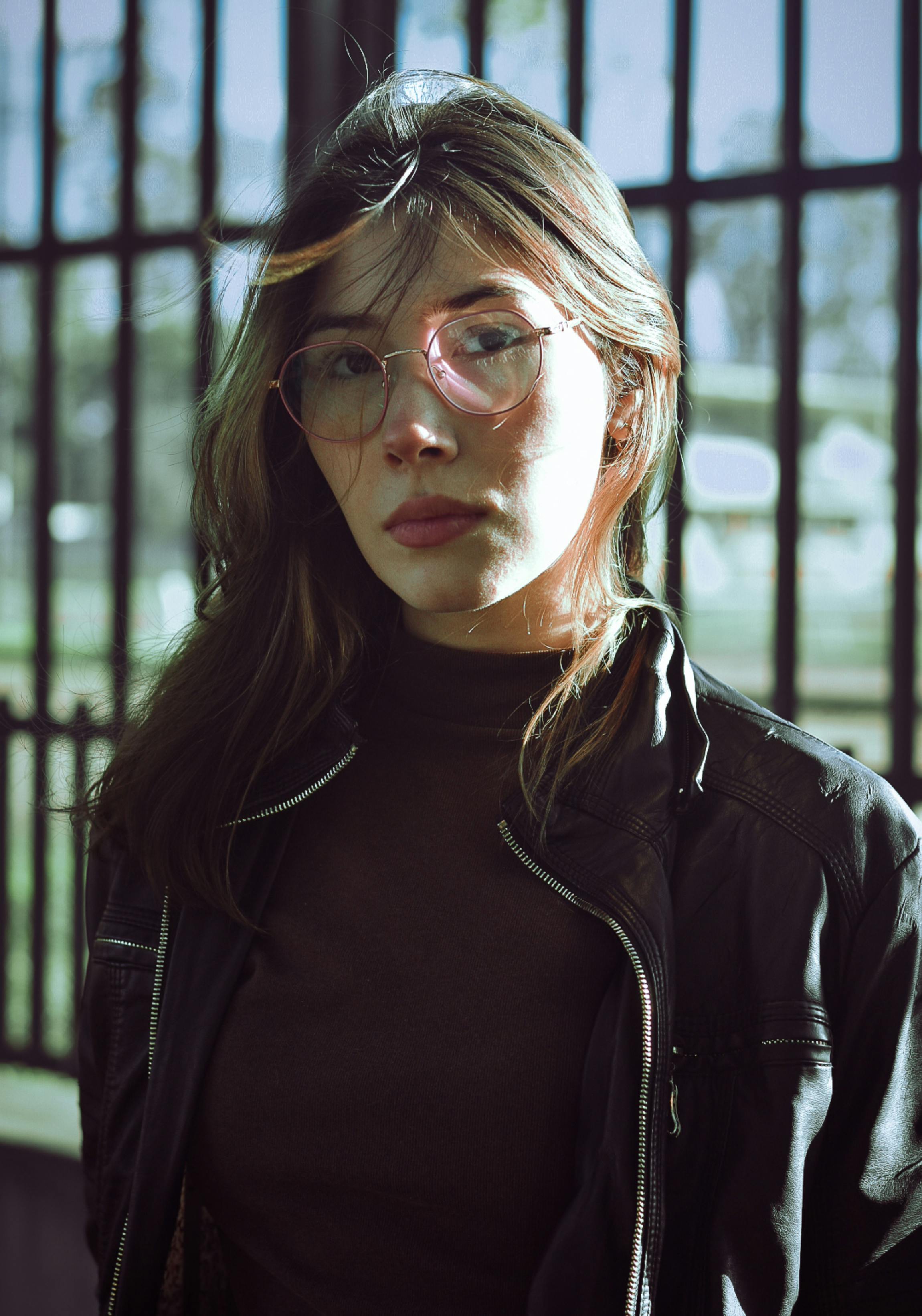 Portrait of a young woman with heart-shaped glasses in a leather jacket outdoors in natural light.