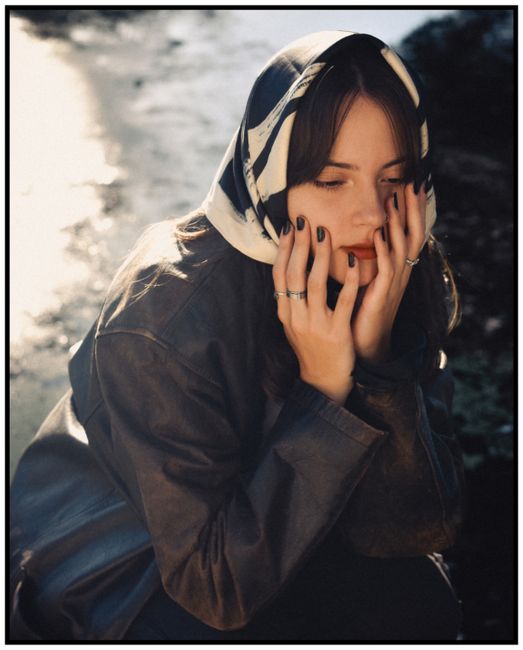 Thoughtful woman in a scarf and jacket sitting by a sunlit outdoors area in Rosario.