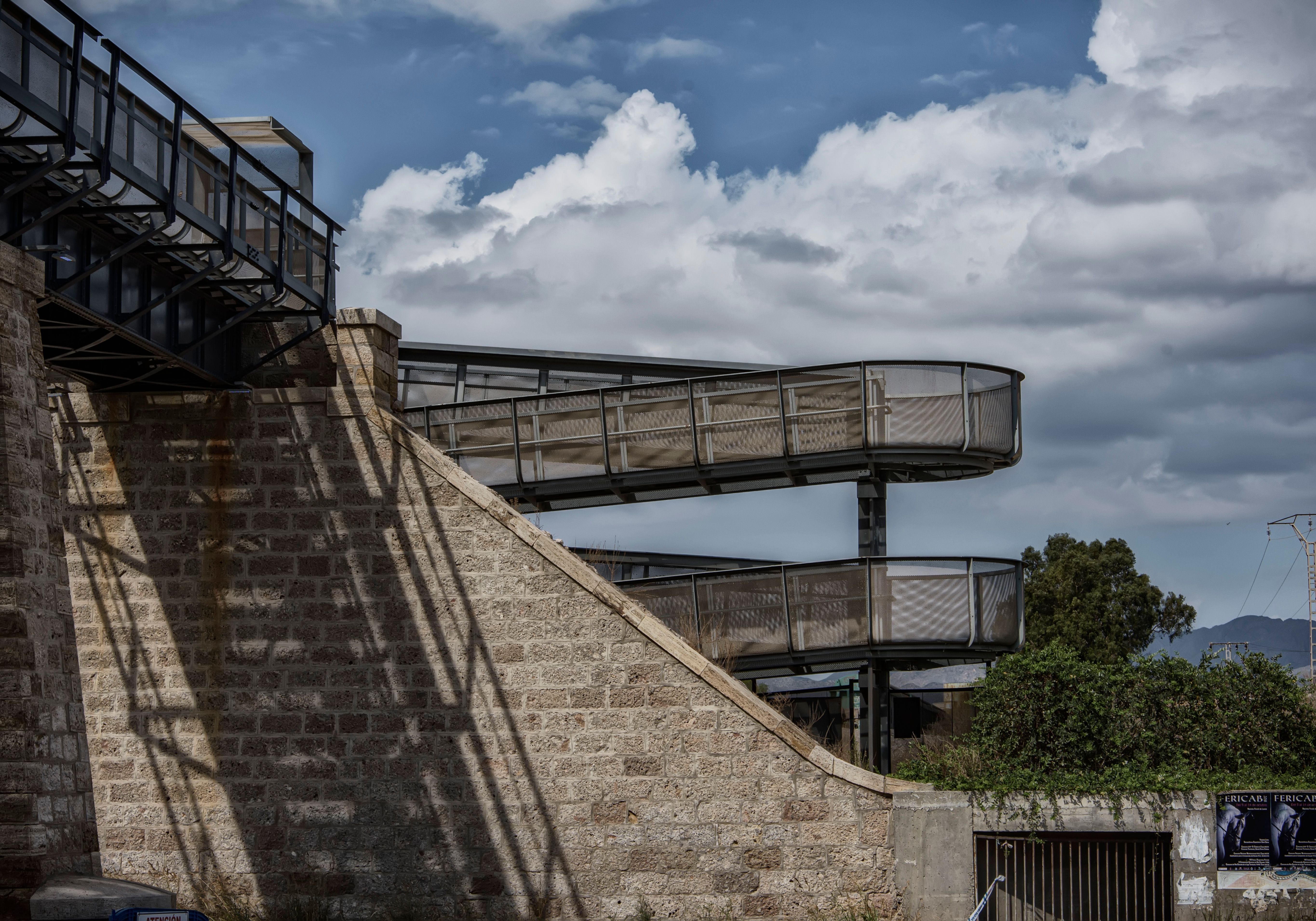 Curved metal walkway with stone wall in Águilas, Spain under a cloudy sky.