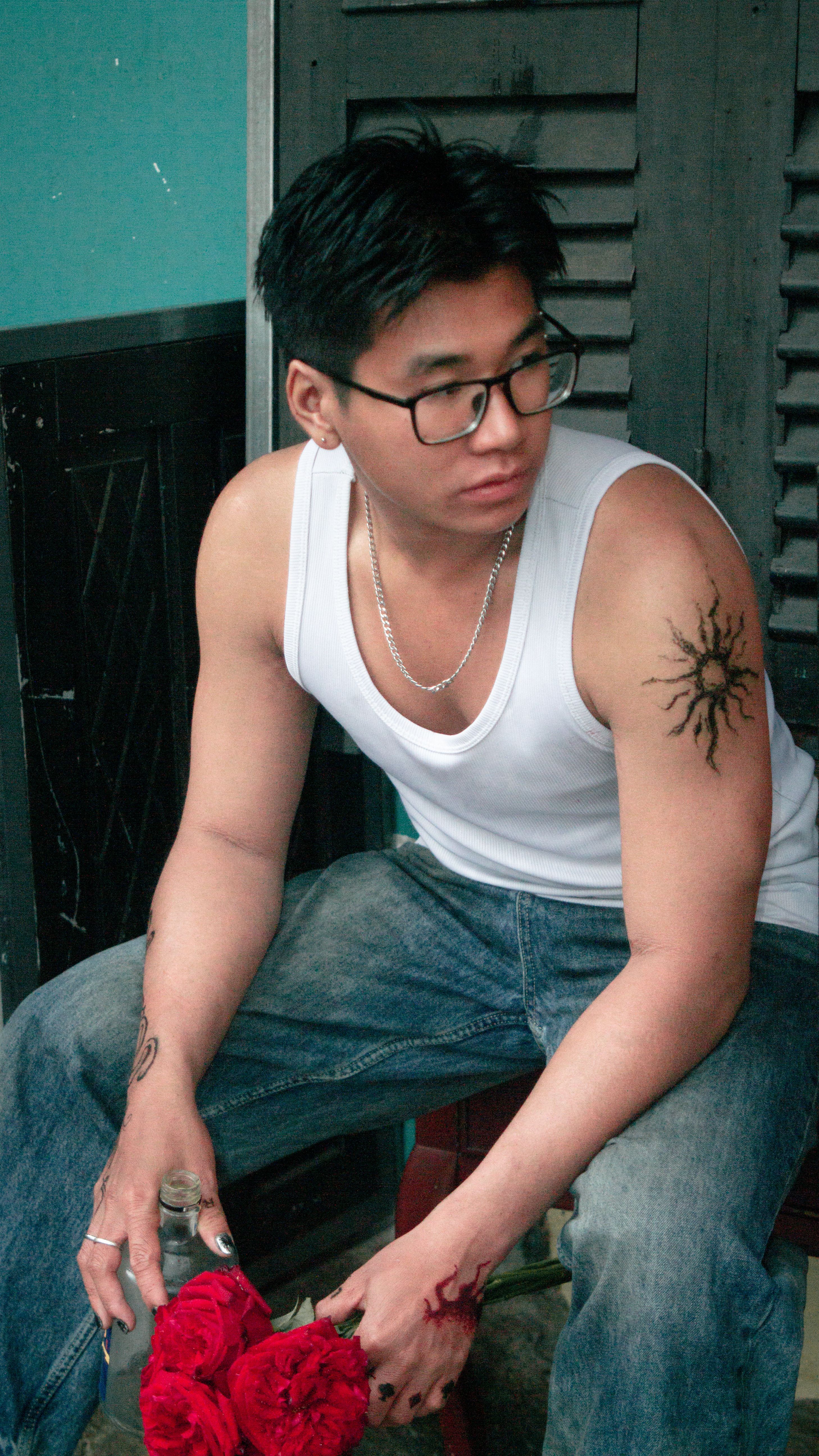 Casual young man with tattoos holding vibrant red roses, seated and gazing into the distance.