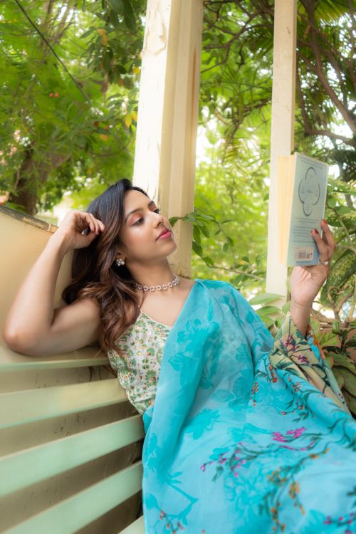 Free Young woman in vibrant sari enjoys reading a book on a sunny balcony. Stock Photo