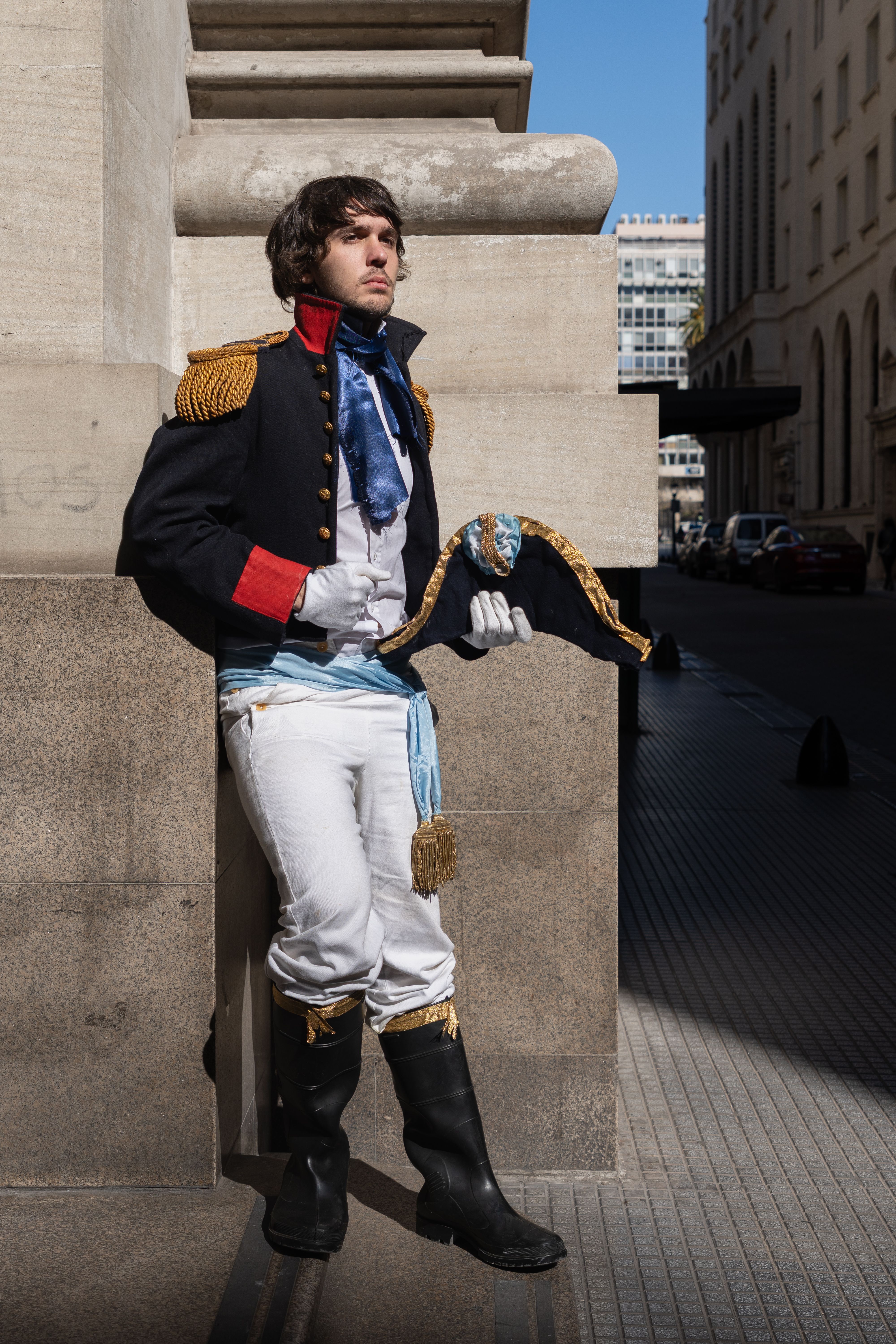 An adult male in a Napoleonic era costume poses against a wall in Buenos Aires.