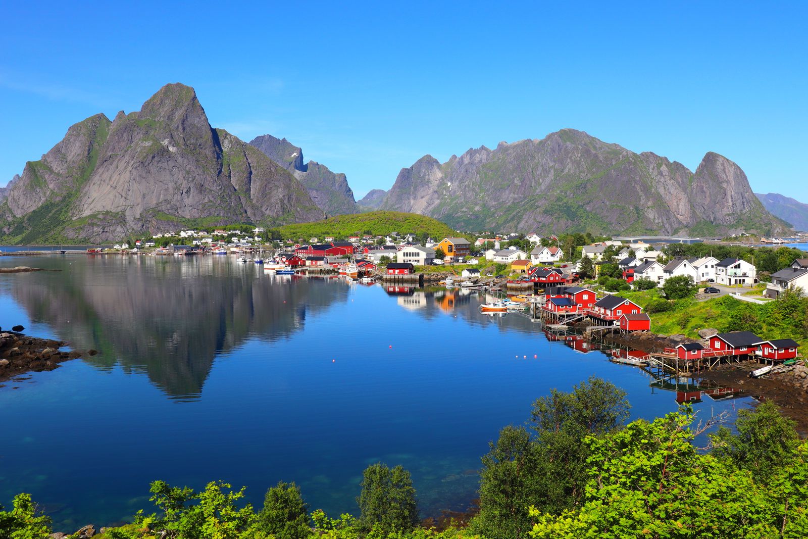 Red cabins of Reine village reflected in calm water beneath Lofoten's jagged peaks