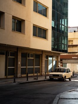 A classic car parked on a quiet city street under modern and vintage architecture.