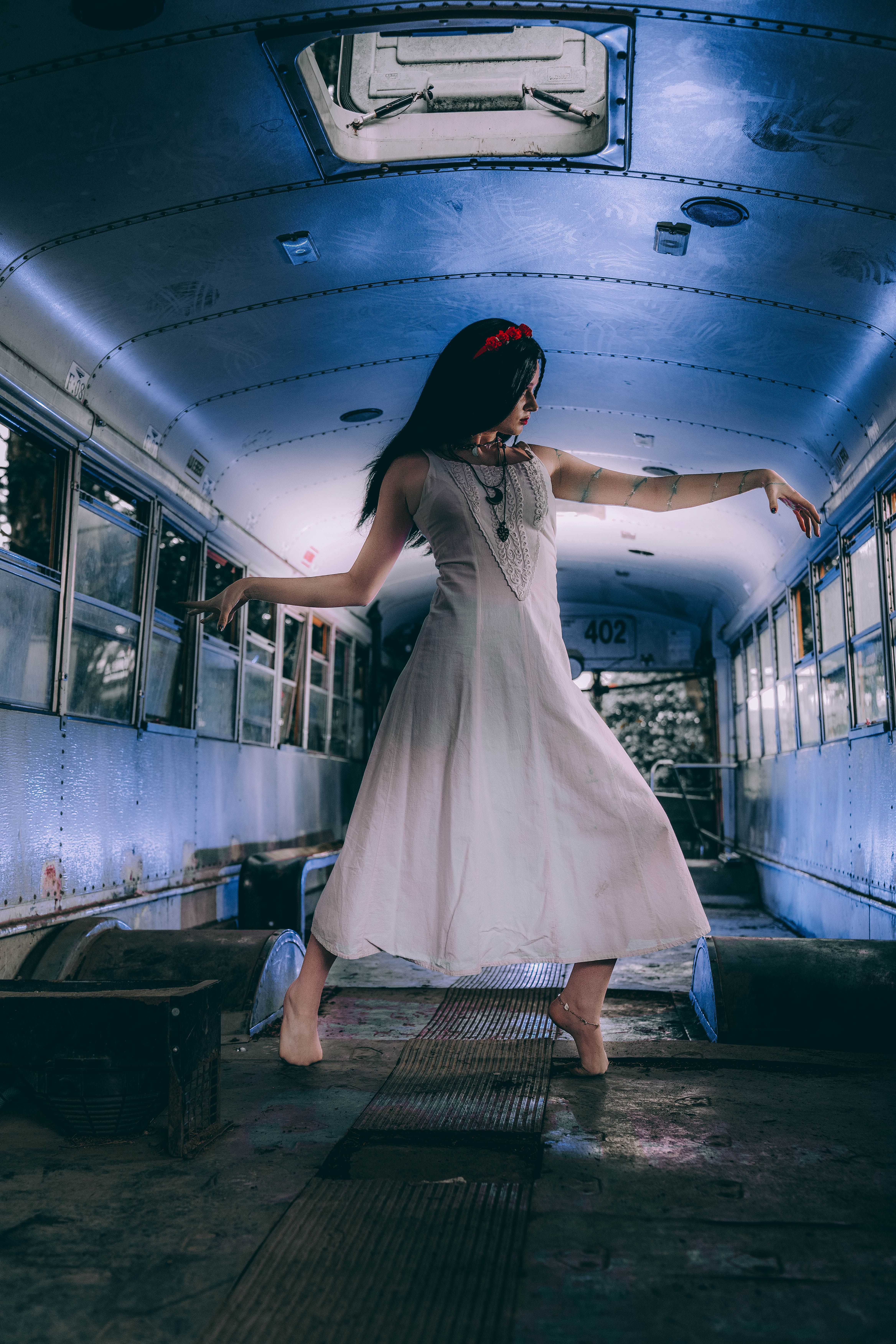 A woman in a white dress gracefully dancing inside an abandoned bus for a dramatic effect.