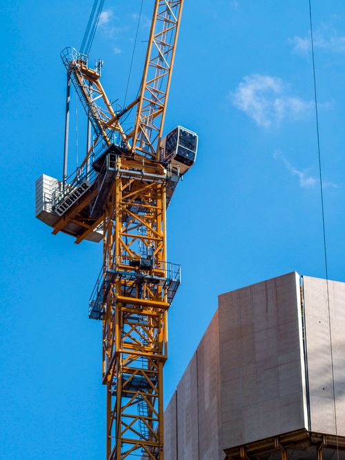 Free Yellow tower crane towering over a construction site against a blue sky with clouds. Stock Photo
