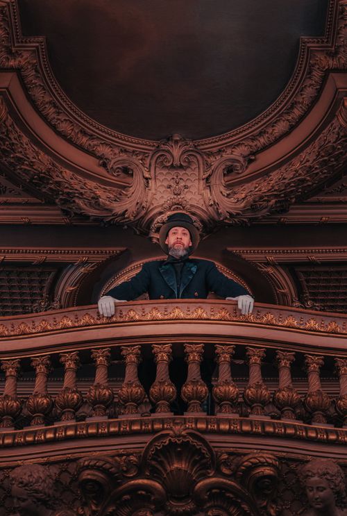 Free A man in formal attire stands on a grand ornately decorated balcony, exuding elegance. Stock Photo