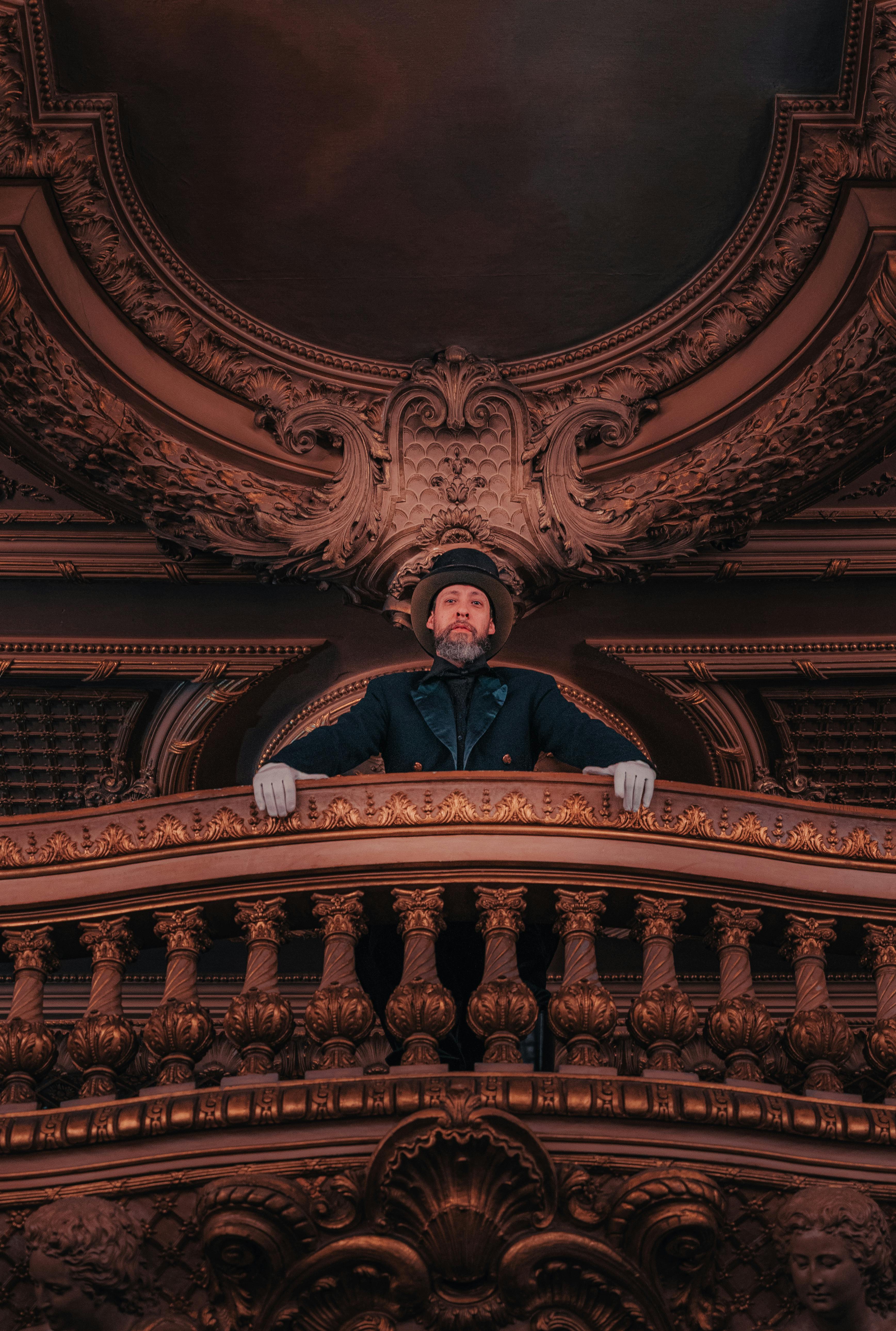 bezplatná Muž ve formálním oděvu stojí na velkolepém zdobeném balkonu a vyzařuje z něj elegance. Základová fotografie