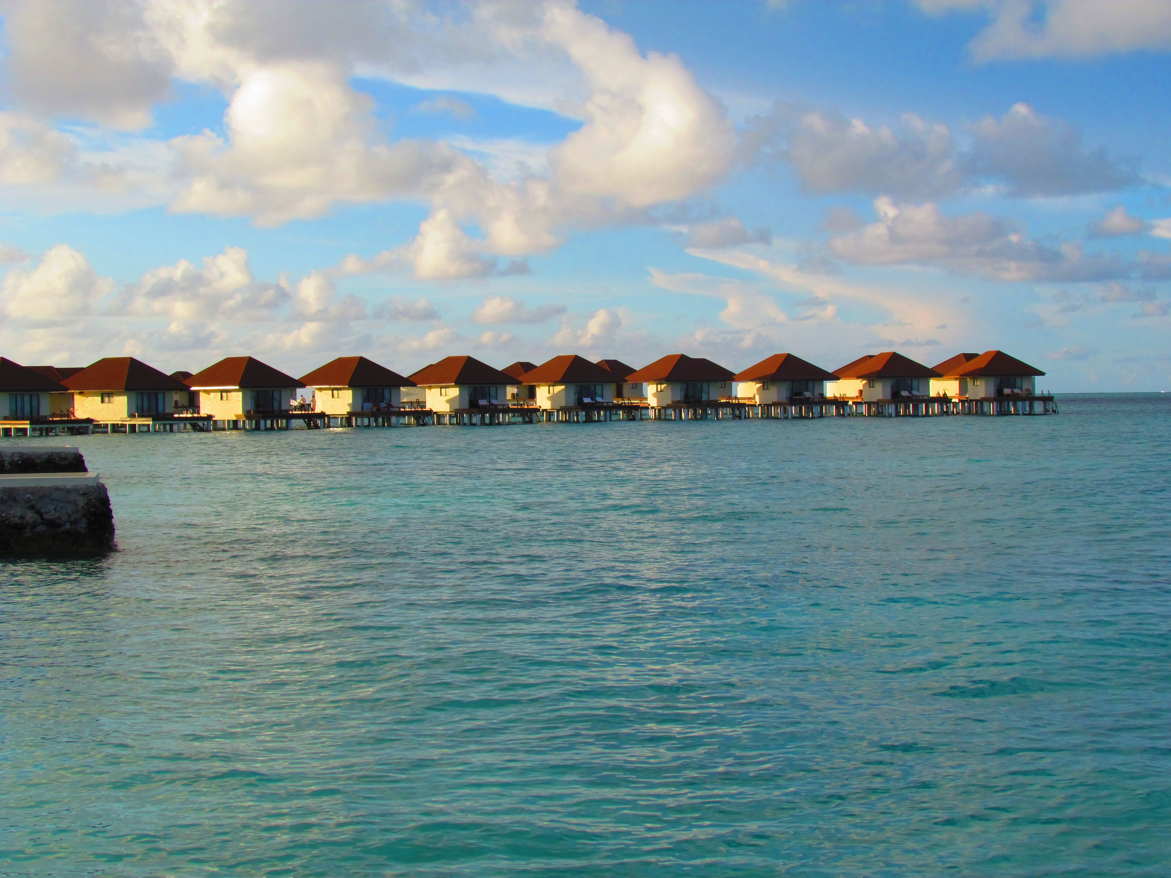 Scenic view of overwater bungalows in Maldives during sunset, showcasing turquoise waters and beautiful skies.