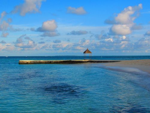 Free Tranquil beach scene in Maldives featuring clear blue waters and a thatched-roof gazebo. Stock Photo