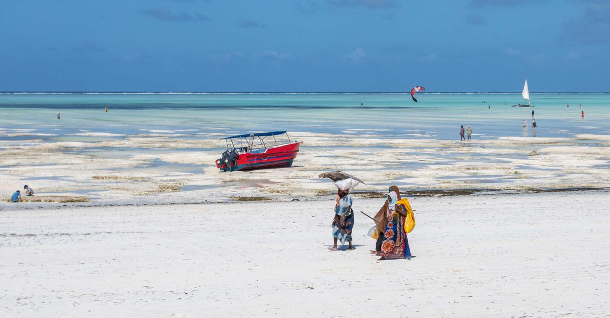 Women walking on a beach in Africa with a vibrant red boat and azure sea.