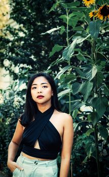 Stylish young woman stands confidently amidst tall sunflowers in a Berlin garden.